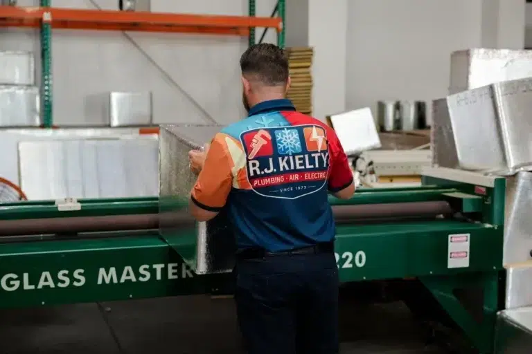 An RJ Kielty technician in a branded uniform preparing tools to service or install a Carrier HVAC unit outdoors