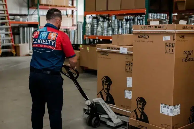 An RJ Kielty technician using a pallet jack to move HVAC equipment in a well-organized warehouse
